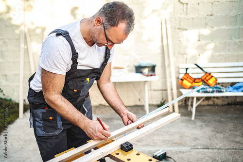 Mature male carpenter measuring wooden plank outdoors photo