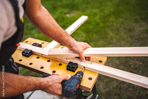 Unrecognizable male carpenter using electric screwdriver on a wooden plank outdoors photo