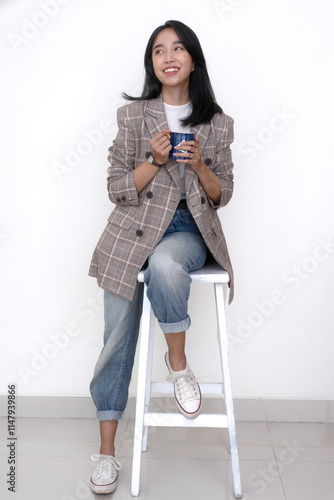 Young Asian woman sitting on white stool holding a cup of hot coffee for breakfast photo