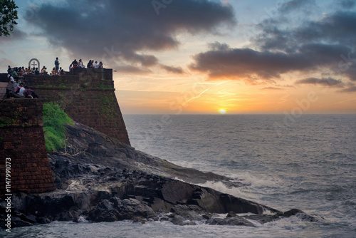Zoomed in shot of tourists enjoying the view at Sinquerim Aguada fort with high monsoon waves at dusk splashing against the huge stone walls of the tower in goa Maharashtra