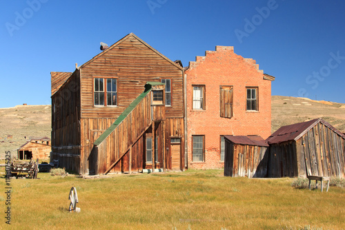 A large, old house with a wooden staircase sits in a grassy field