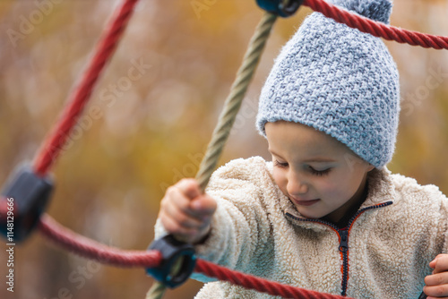 Child playing on a rope climbing structure at a playground in autumn. Estilo de vida, Crianza. photo