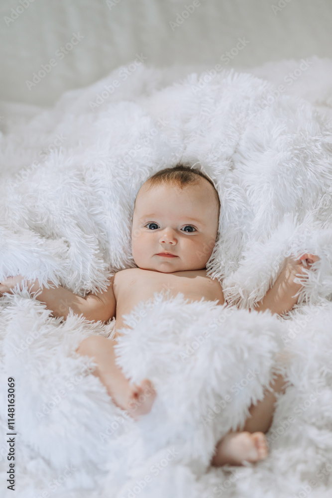A baby is laying on a white blanket. The baby is looking at the camera A baby is laying on a white blanket. The baby is looking at the camera