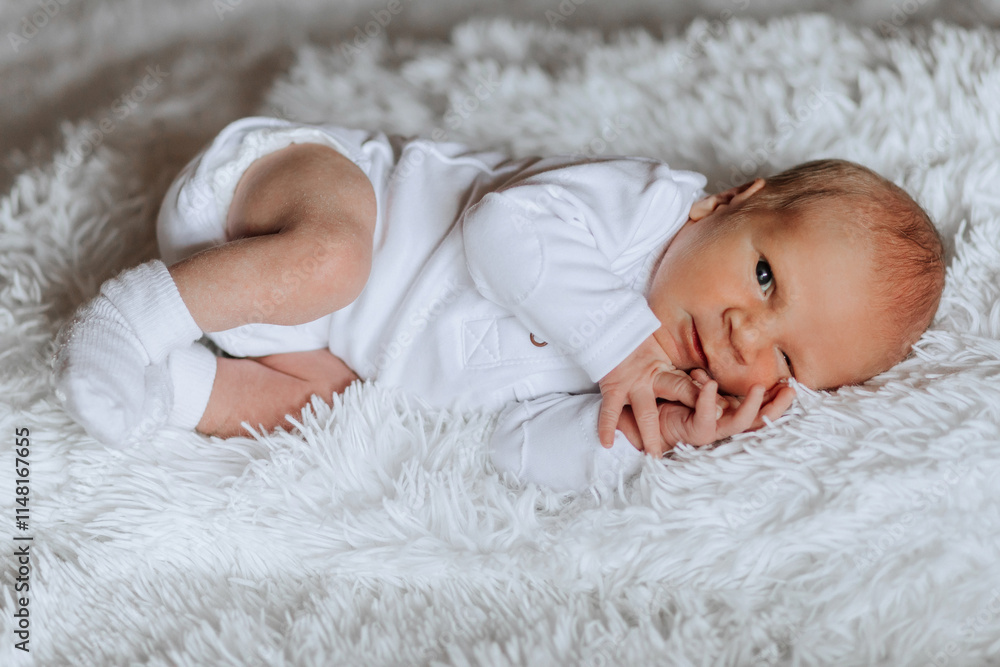 A baby is laying on a white blanket. The baby is wearing a white onesie and has a white sock on. The baby is looking at the camera with a smile A baby is laying on a white blanket. The baby is wearing a white onesie and has a white sock on. The baby is looking at the camera with a smile