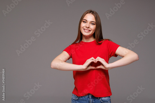 Smiling pretty woman showing heart gesture with hands while standing isolated over gray background