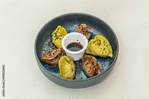 A black bowl with a blue bottom filled with multi-colored gyozas, poppy seeds and soy sauce. photo