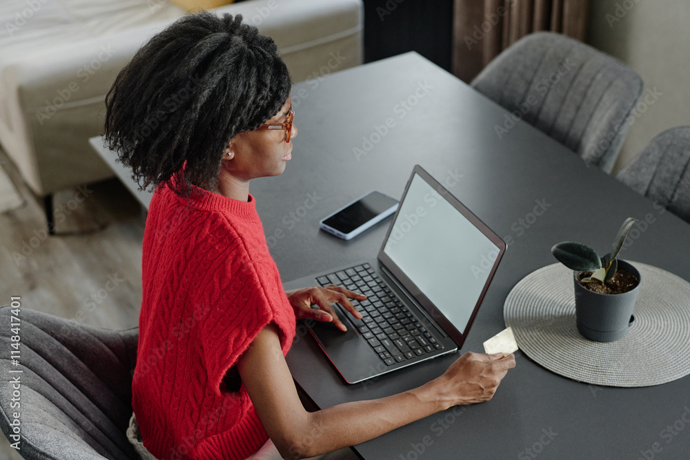High angle shot of elegant African American woman sitting on chair and focused on online shopping at home High angle shot of elegant African American woman sitting on chair and focused on online shopping at home