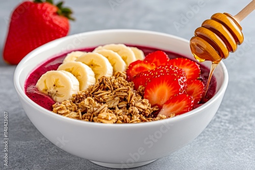 A colorful acai bowl topped with sliced bananas, strawberries, granola, and a drizzle of honey, served in a white ceramic bowl photo