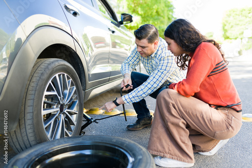 Dad teaching his teenage daughter essential car maintenance skills by demonstrating how to change a flat tire photo