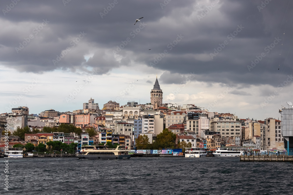 Fototapeta premium Iconic Galata Tower at sunset in Istanbul, Turkey. Distinctive conical shape and golden spire, stands tall against dramatic sky with fluffy clouds. Bustling cityscape with rooftops and buildings