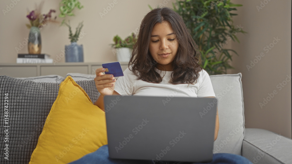 A young hispanic woman shopping online with a credit card on her laptop in a cozy living room, featuring greenery and stylish decor. A young hispanic woman shopping online with a credit card on her laptop in a cozy living room, featuring greenery and stylish decor.