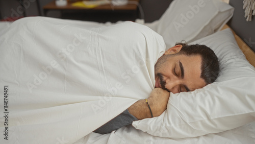 Young hispanic man with a moustache sleeping comfortably in bed in a cozy bedroom at home.