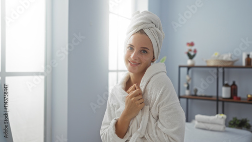 Woman relaxing at a spa wrapped in a towel, smiling with a serene expression in a bright, peaceful wellness center with shelves in the background and sunlight streaming through large windows