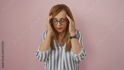 Beautiful elderly blonde woman in glasses and striped shirt with hands touching head over pink background