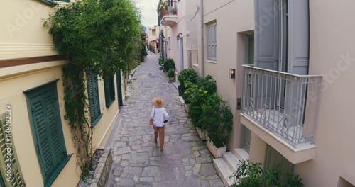 Tourist woman with hat walking sightseeing an beautiful street in the old district of Plaka in Athens, Greece, aerial drone tracking shot
