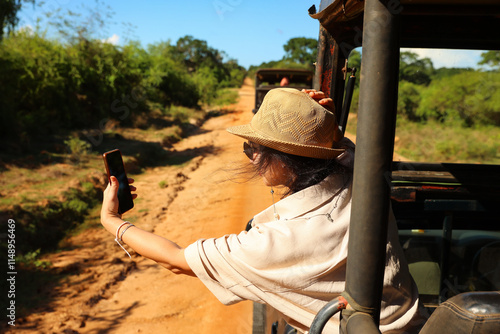 A girl in a hat rides a jeep and takes a selfie. Safari Sri Lanka.