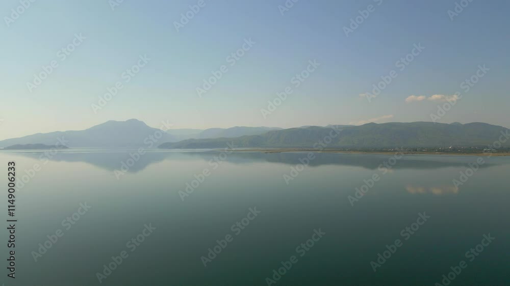 A serene natural landscape with a lake reflecting the sky, surrounded by misty mountains in the background. A serene natural landscape with a lake reflecting the sky, surrounded by misty mountains in the background.