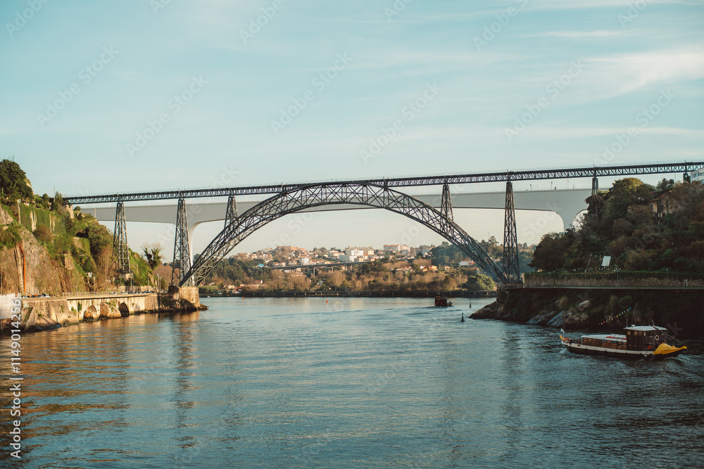 Fototapeta premium The Dona Maria Pia Bridge spans the Douro River in Porto, Portugal, showcasing an elegant iron arch design, historic engineering, and scenic views of the surrounding area