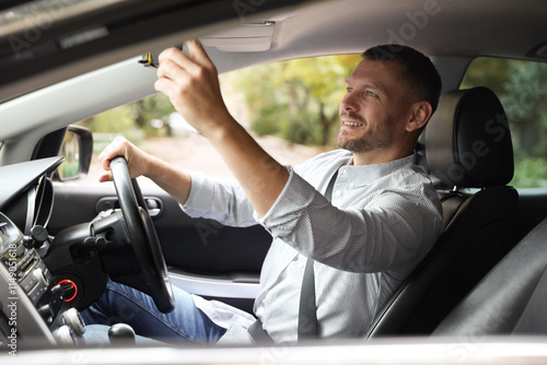 Man adjusting rear-view mirror in car before driving photo