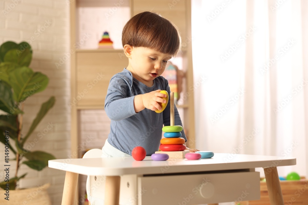 Cute little boy playing with toy pyramid at table indoors Cute little boy playing with toy pyramid at table indoors