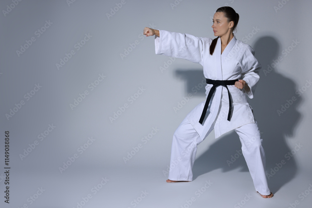 Young woman in kimono practicing karate on grey background, space for text Young woman in kimono practicing karate on grey background, space for text