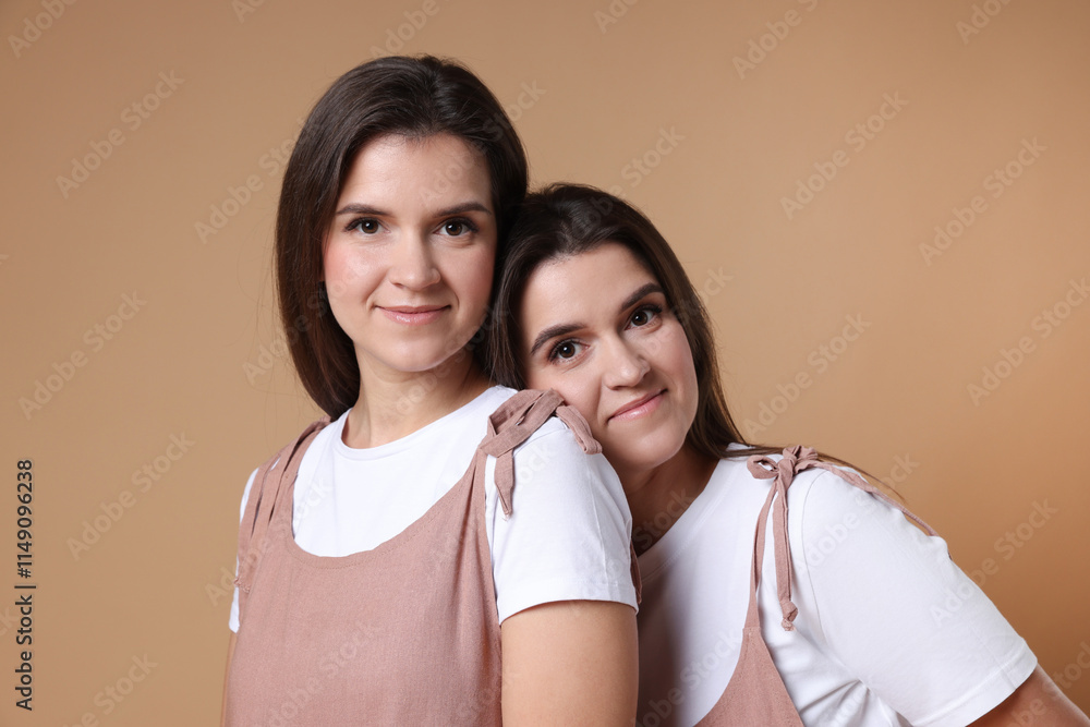 Portrait of beautiful twin sisters on pale brown background Portrait of beautiful twin sisters on pale brown background