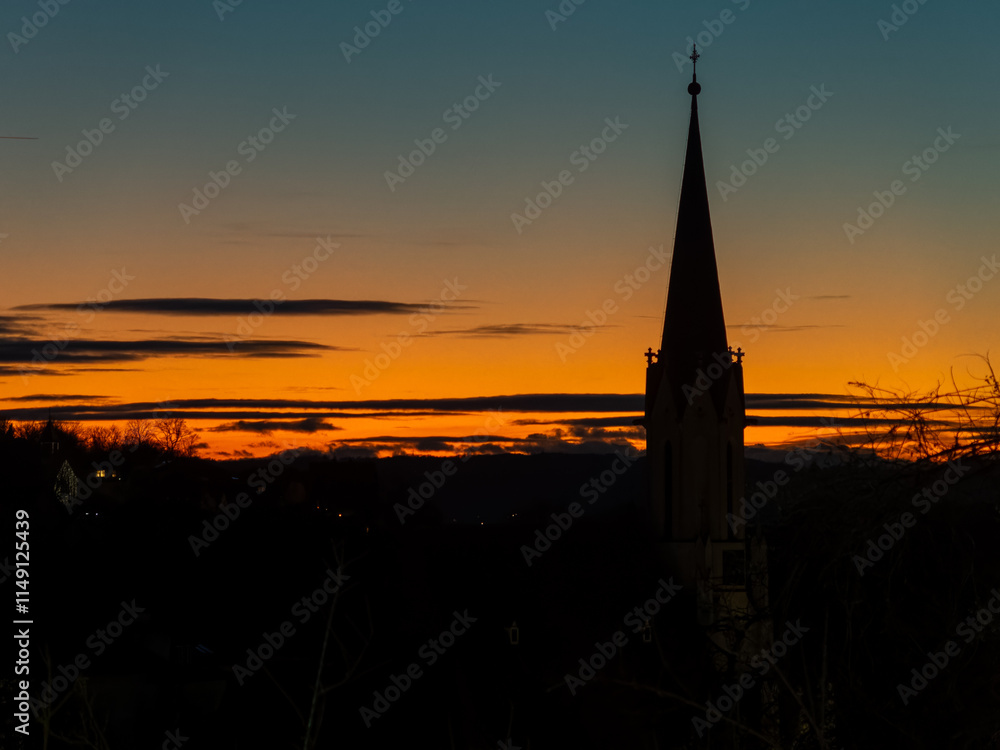 Obraz premium Golden sunset silhouetting a church spire against a colorful sky in the evening hours