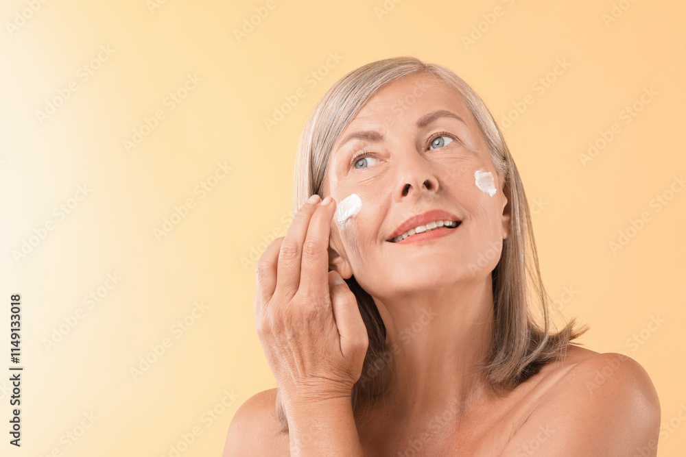 Senior woman applying face cream on beige background. Space for text Senior woman applying face cream on beige background. Space for text