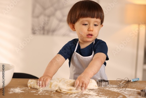 фотографія Cute little boy kneading dough at wooden table indoors