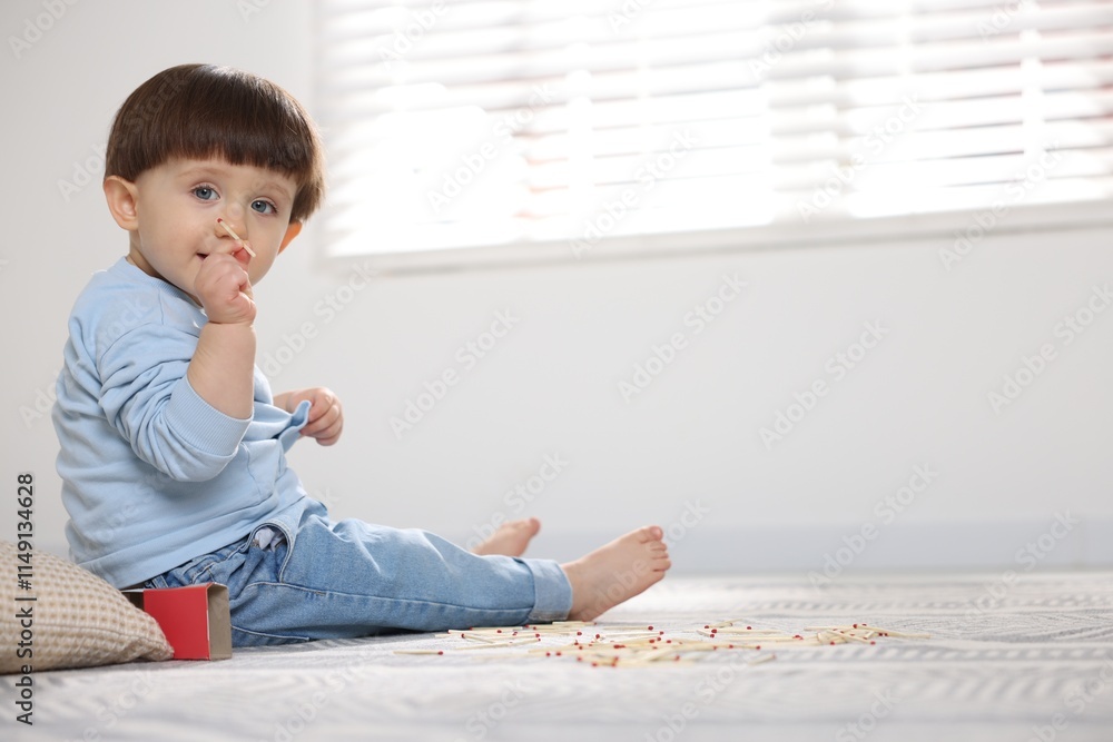 Fototapeta premium Little boy playing with matches at home, space for text. Child in danger