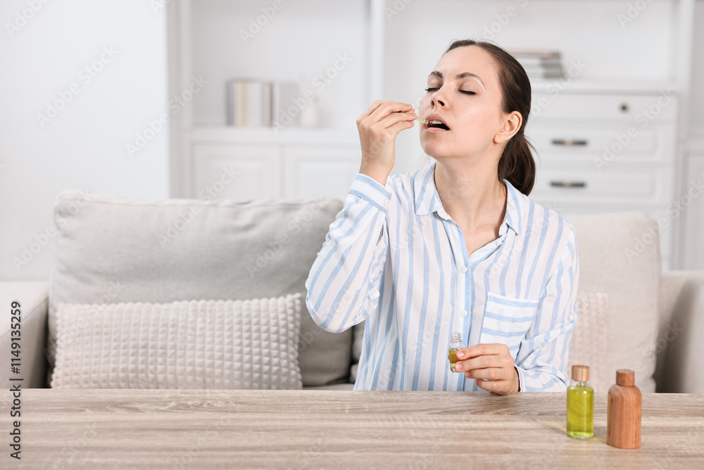 Young woman taking CBD tincture at wooden table indoors, space for text Young woman taking CBD tincture at wooden table indoors, space for text