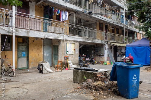 Photography a lower-income neighborhood in China with decaying and weathered residential apartment buildings, a fallen trash bin, and a dirty and messy communal area