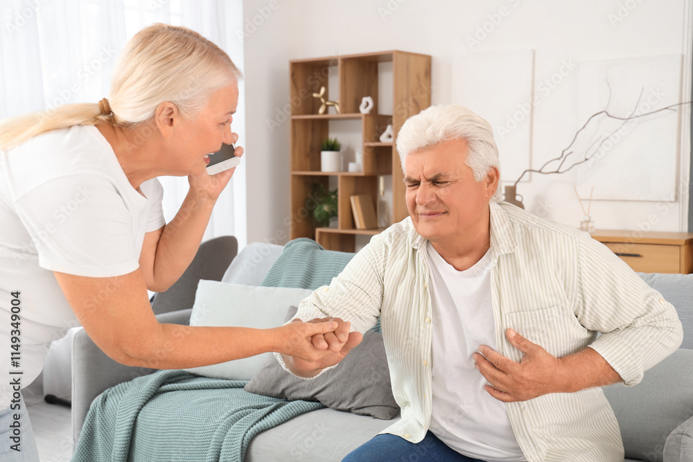 Fototapeta premium Mature woman calling ambulance for her husband having heart attack on sofa at home