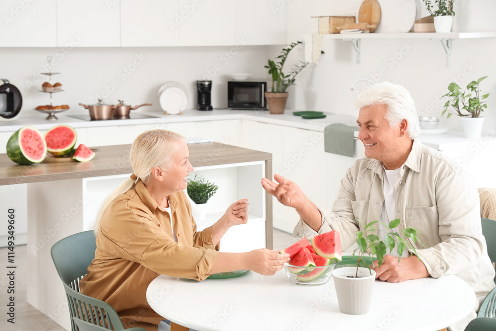 Mature couple with slices of fresh watermelon at table in kitchen Mature couple with slices of fresh watermelon at table in kitchen