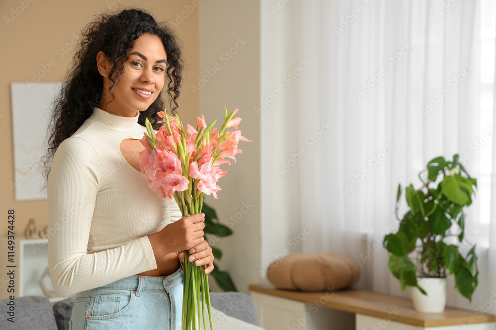 Beautiful young happy African-American woman with bouquet of pink gladiolus flowers at home