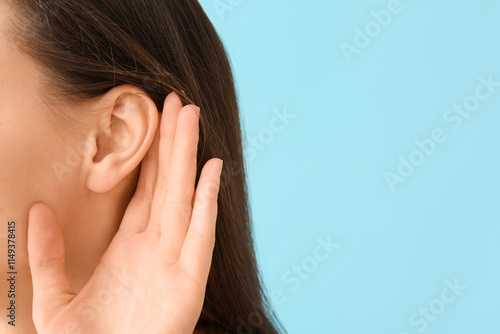 Young gossip woman trying to hear something on blue background, closeup photo