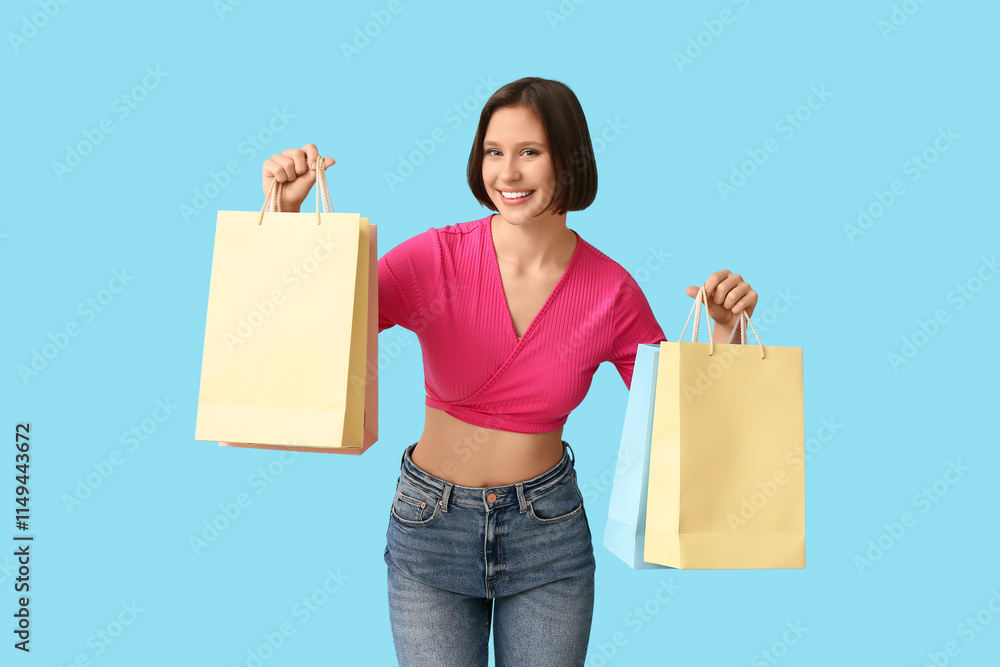 Young woman in stylish t-shirt with shopping bags on blue background Young woman in stylish t-shirt with shopping bags on blue background
