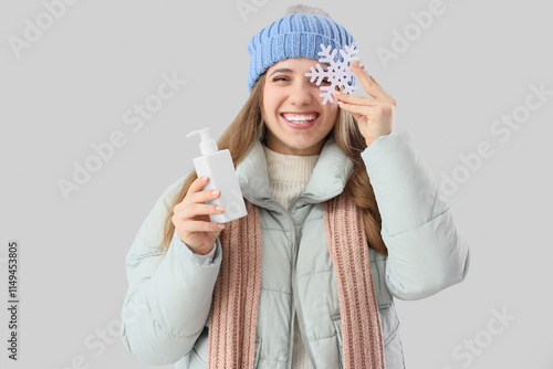 Happy woman in winter clothes, with cosmetic cream and snowflake on grey background photo