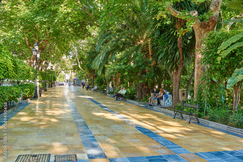 Obraz premium Park, travel and walkway with tourist people at Parque de la Alameda in Marbella, Spain. Nature, trees and spring with brick lane road outdoor in conservation location for sightseeing or tourism