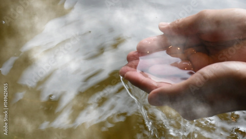 湯けむりが立つ檜の露天風呂に入浴する男性が湯を手ですくうシーン
