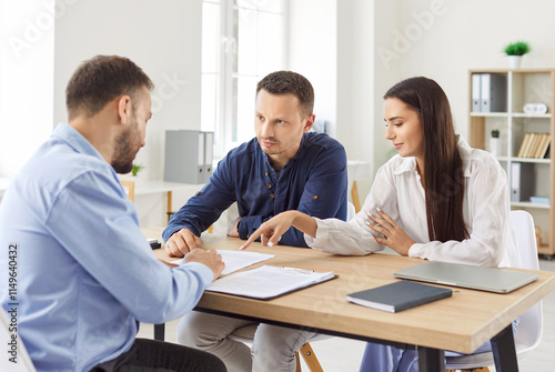 Young caucasian couple sitting at the desk discussing contract and having consultation with man realtor or financial advisor in office. Insurance agent consulting man and woman in office.