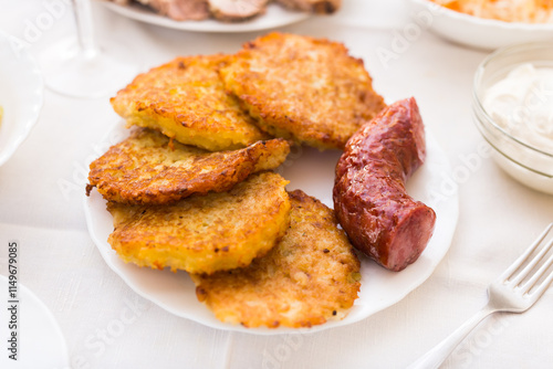 Potato pancakes with fried sausage on white plate photo