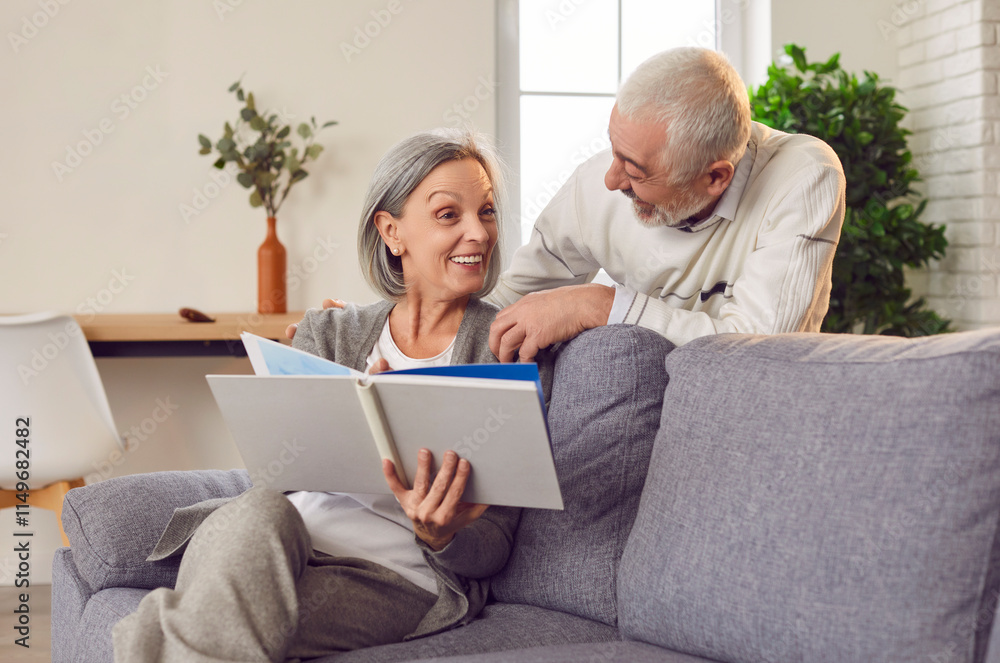 Portrait of a happy cheerful senior elderly couple looking through a family photo album sitting on sofa in living room at home. Mature married man and woman enjoying leisure time together. Portrait of a happy cheerful senior elderly couple looking through a family photo album sitting on sofa in living room at home. Mature married man and woman enjoying leisure time together.