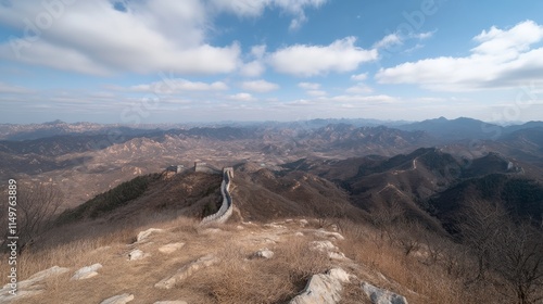 Panoramic View of the Great Wall of China Stretching Across Mountains Under a Blue Sky with Clouds and Barren Trees in the Foreground, Capturing Natural Beauty and History