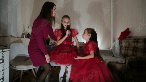 Mother and little daughters celebrating birthday, singing microphone at home