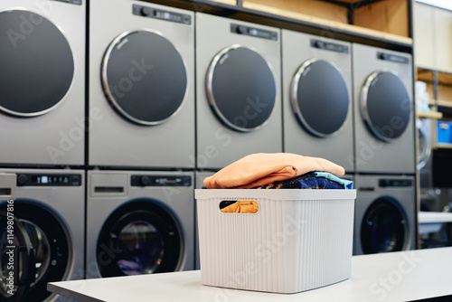 Still life shot of basket full of clean and fresh clothes on folding table in self service laundry with professional washing machines, copy space photo