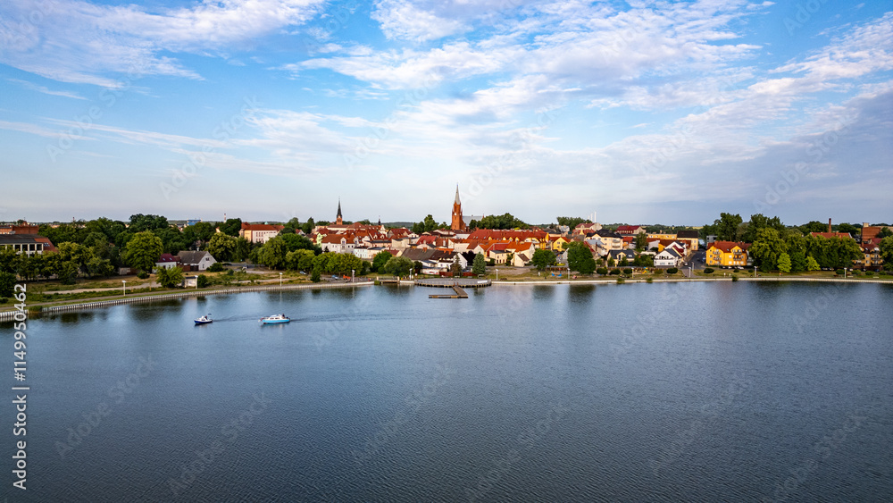 Obraz premium Picturesque Lake Raduń in Wałcz, Poland. Tranquil waters of Lake Raduń with colorful town buildings, scenic promenade, and boats gliding on the surface in Wałcz, Poland.