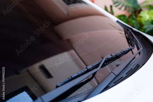Section of the front of a white vehicle and its front windscreen bonnet and wipers.