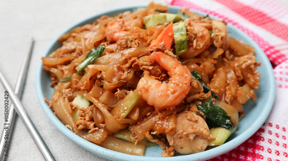 Kwetiaw or Kwetiau seafood, fried rice noodles with prawn or shrimp and vegetables. Popular in Indonesia served on blue plate isolated on grey. close up Kwetiaw or Kwetiau seafood, fried rice noodles with prawn or shrimp and vegetables. Popular in Indonesia served on blue plate isolated on grey. close up