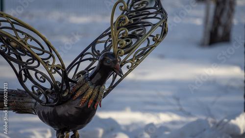 Bronze sculpture of fabulous bird in city park Manin Park in city of Verkhnyaya Pyshma on winter day against backdrop of snow photo